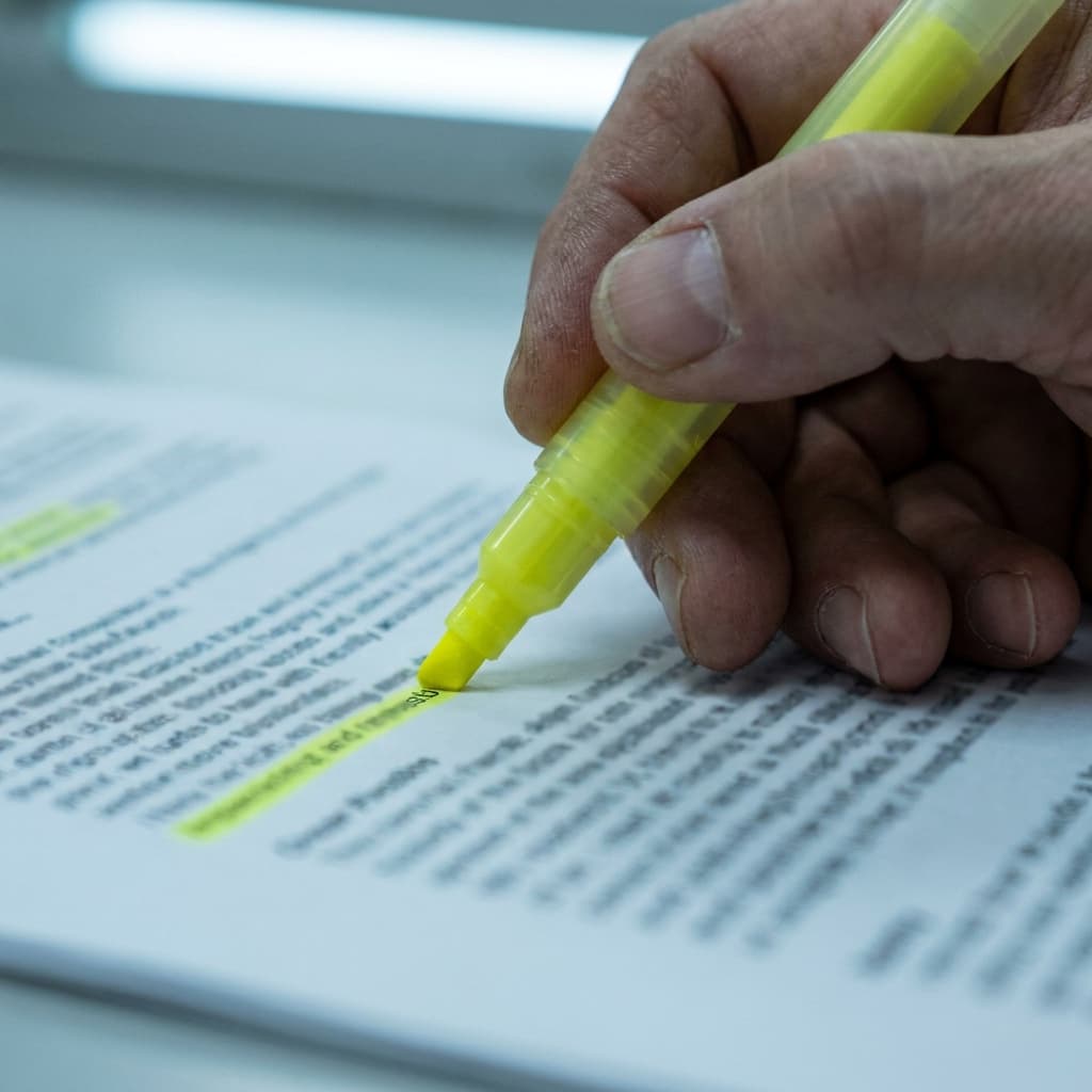 Close-up of a hand using a yellow highlighter on a dense block of printed text on paper.